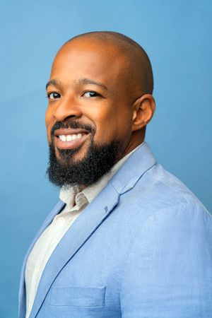 Professional headshot of person in light blue blazer against blue background.