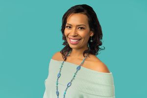 Portrait of person in off-shoulder sweater with turquoise necklace against teal background.