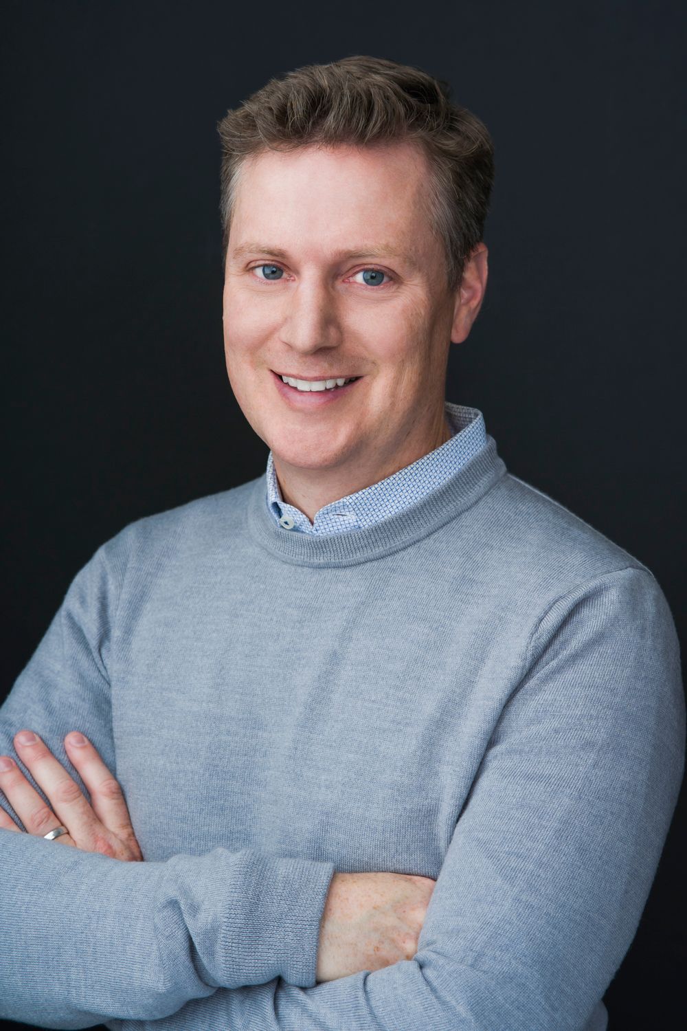 Professional headshot of person in light gray sweater against dark background.