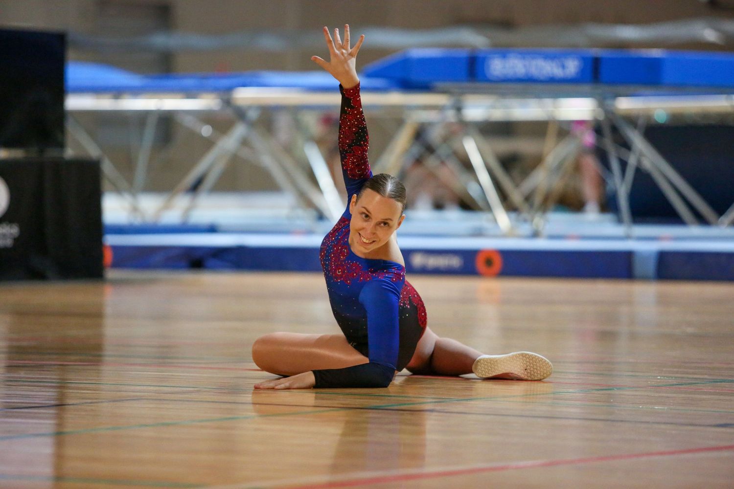 Gymnast in red and blue leotard performs floor routine in split position.