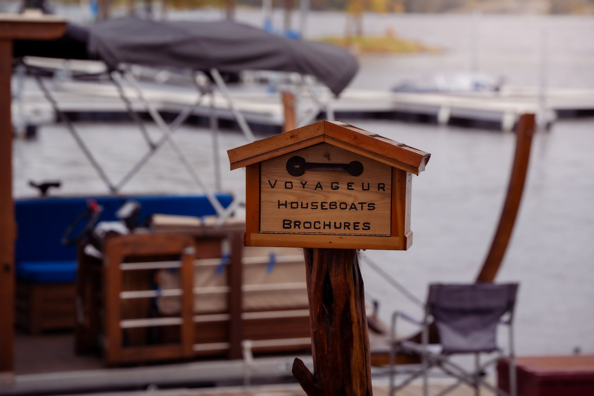 Wooden sign for Voyageur houseboats mounted on post at marina dock.