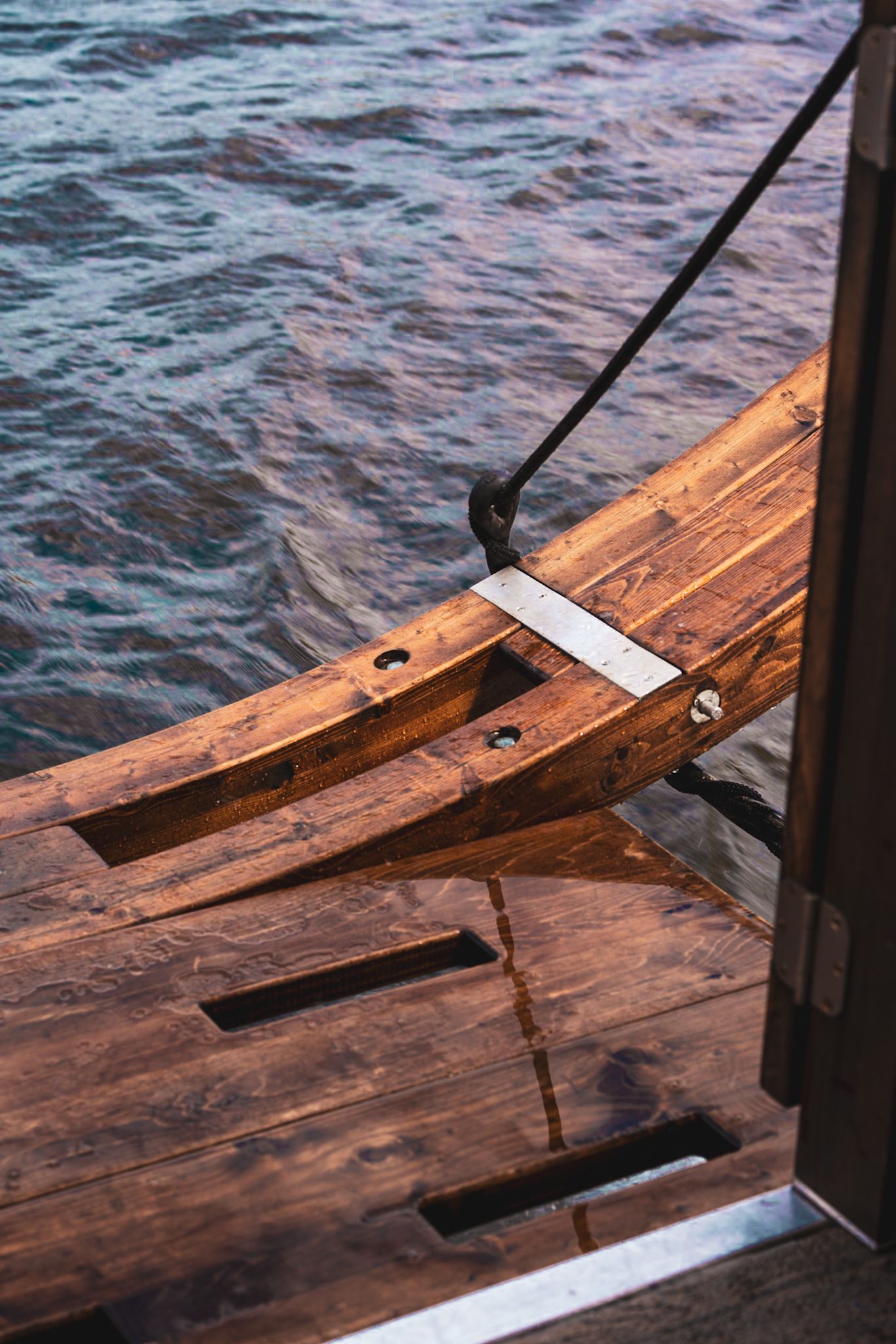 Close-up of wooden boat deck and railing against rippling water.