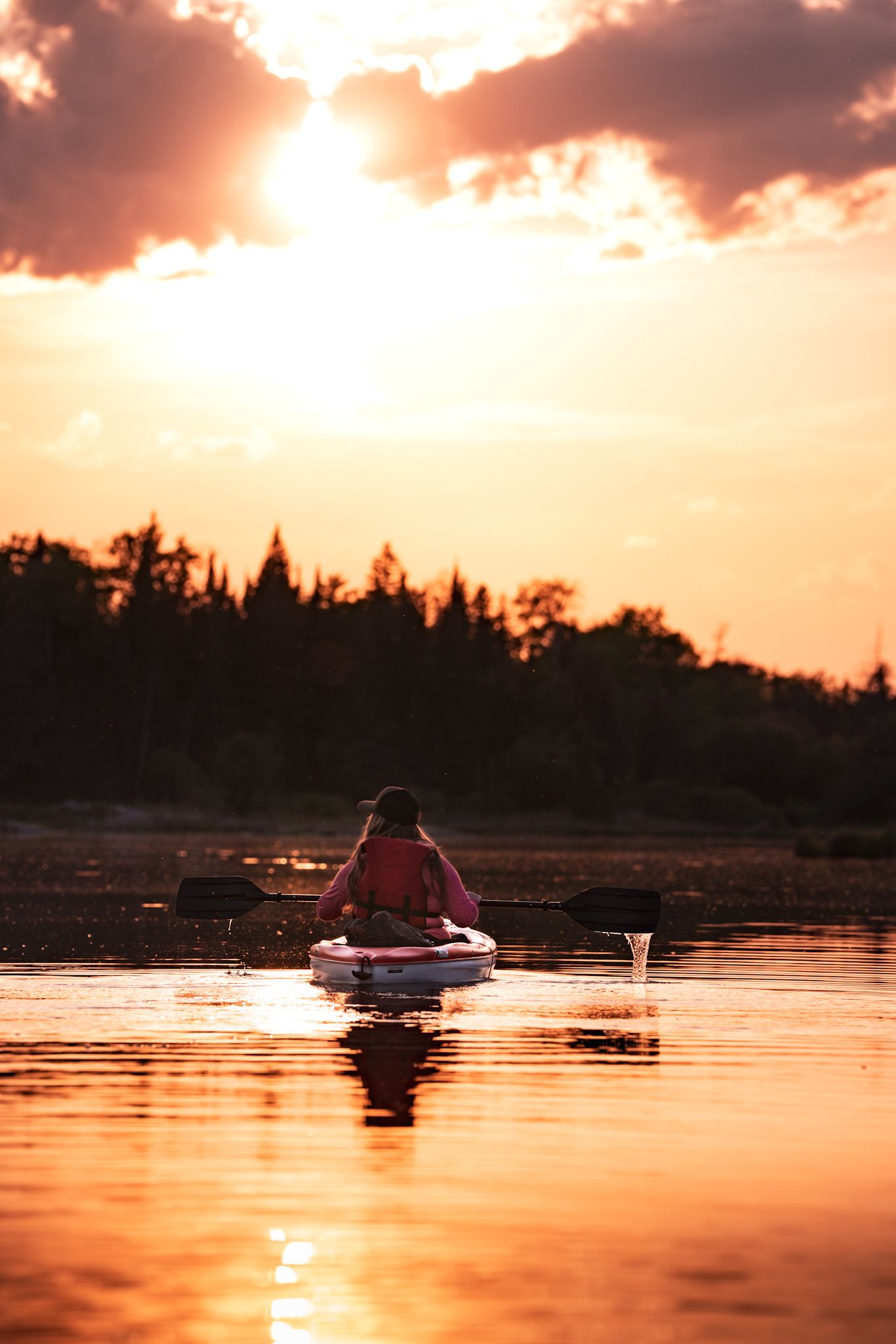 Paddler on kayak silhouetted against dramatic orange sunset sky.