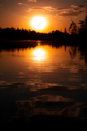 Dramatic sunset reflection over calm lake with treeline silhouette.
