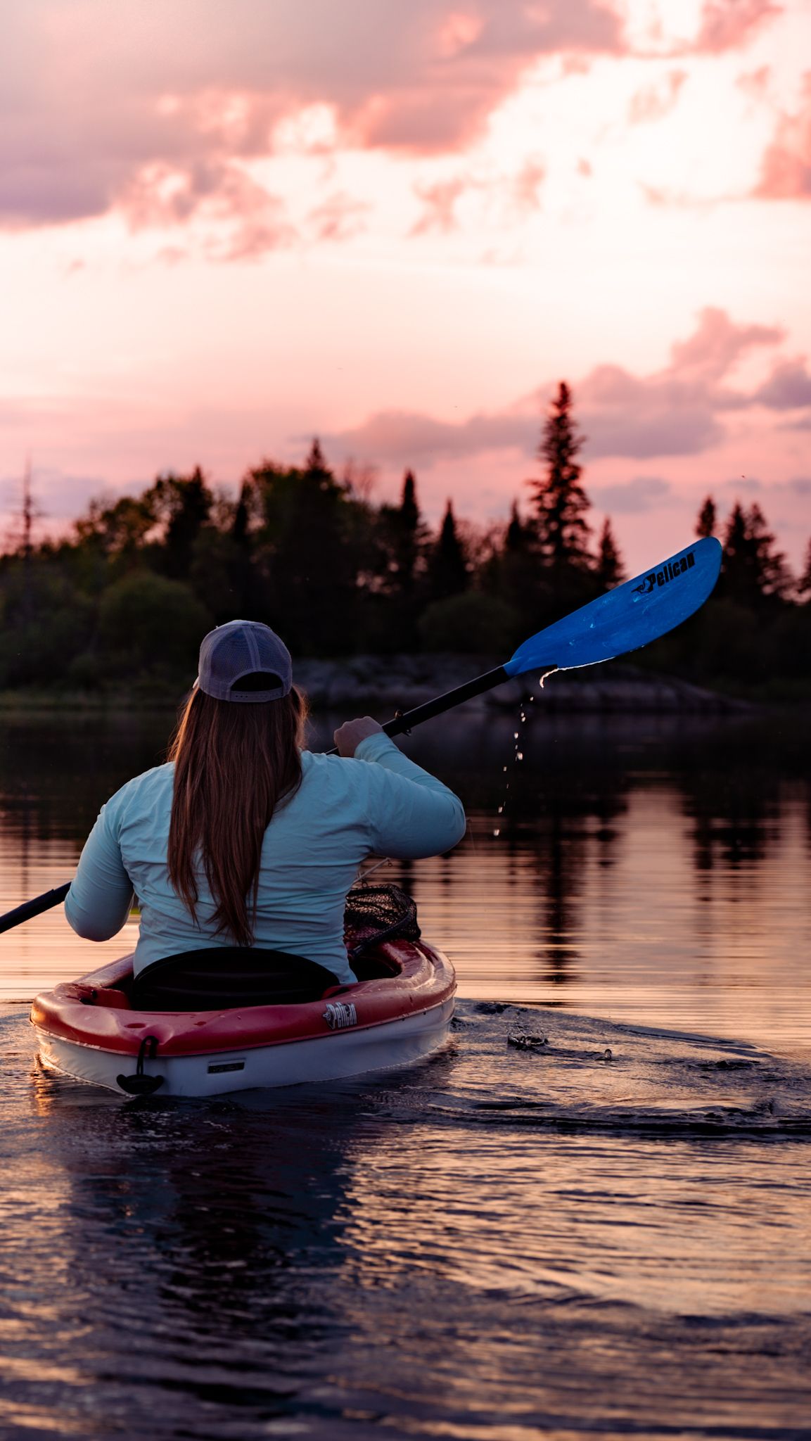 Kayaker paddling on calm lake waters during pink sunset.