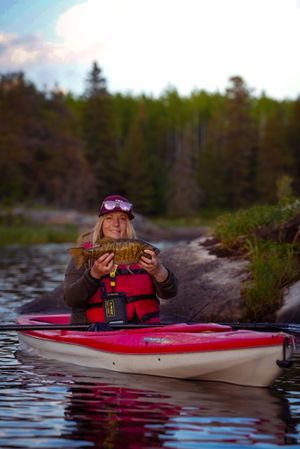 Kayaker on red and white kayak displays caught fish on calm lake waters.