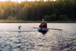 Kayaker fishing at golden hour with jumping fish visible in background.
