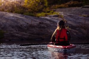 Kayaker in red life vest paddling on calm lake waters during golden sunset.