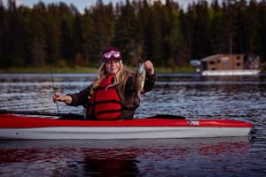 Kayaker wearing red life jacket showing catch while fishing from red kayak on lake.