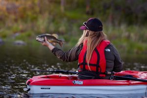 Angler in red life vest displays caught fish from kayak on peaceful lake.