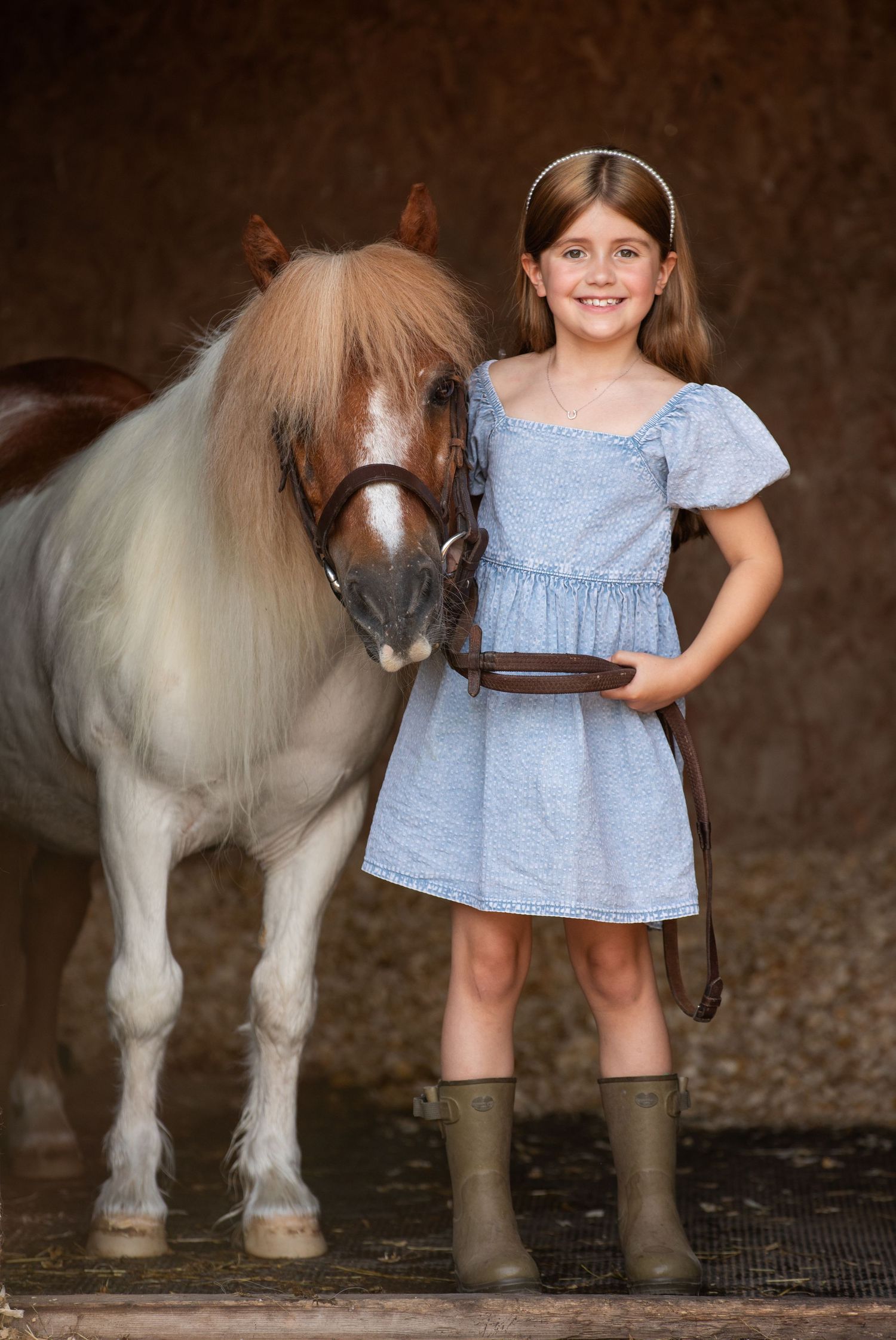 Young girl in denim overalls embraces a palomino horse in a sun-dappled forest setting.