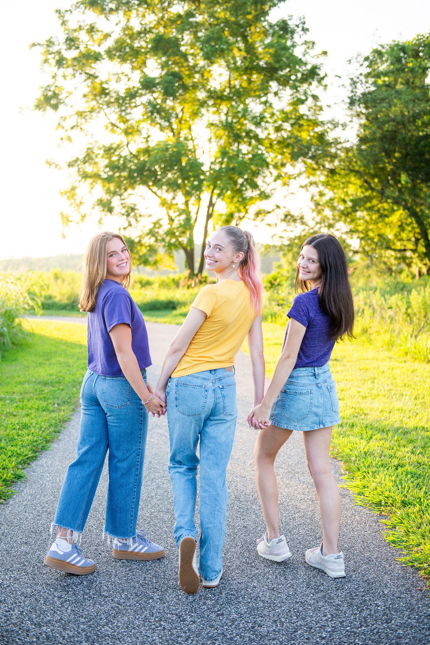 Three people in denim walking away on a countryside path during golden hour sunset.