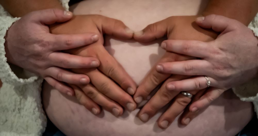 Two pairs of hands interlinked with fingers intertwined on a light colored surface.