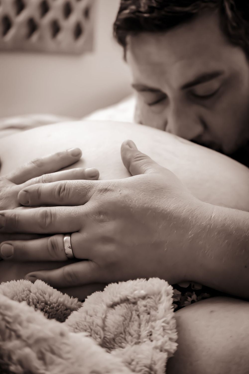 Black and white photo showing someone resting with their hand on a soft blanket, wearing a wedding ring.