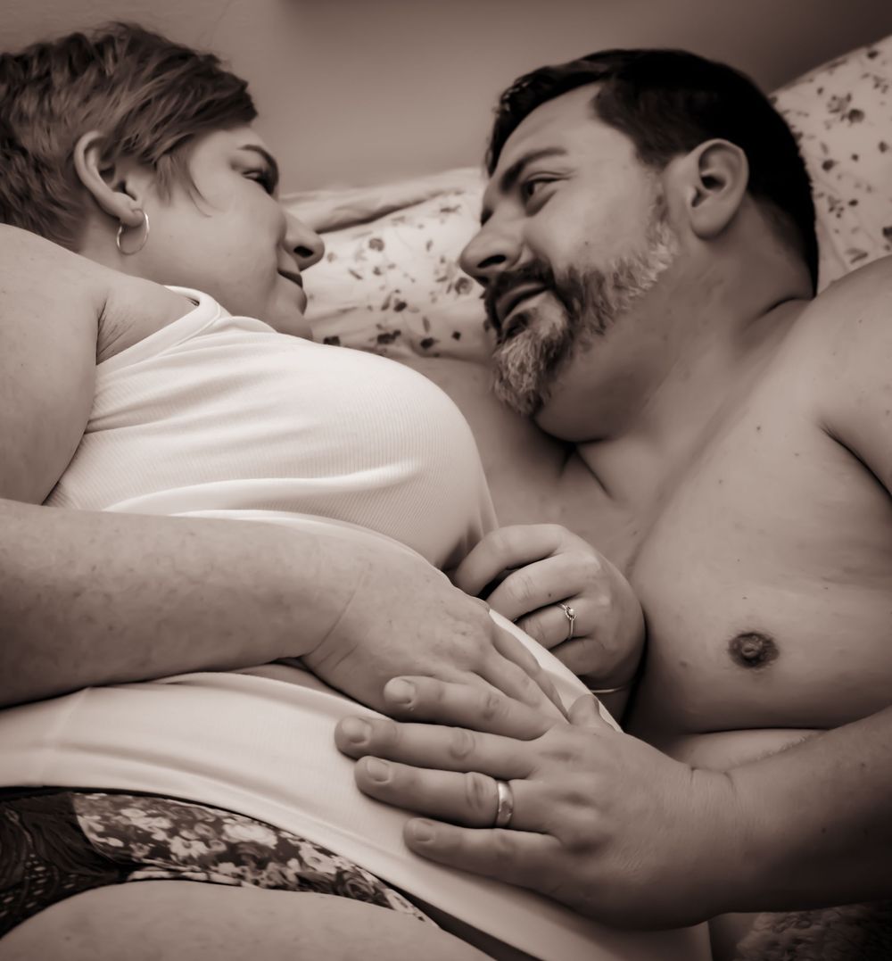 A tender monochromatic photo of a couple sharing an intimate moment together while lying in bed.