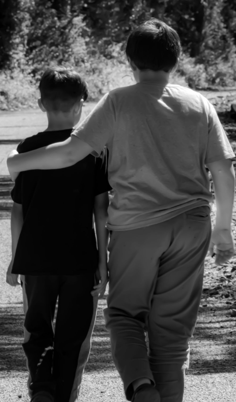 A black and white photo showing two people walking together on a path with one's arm around the other's shoulder.
