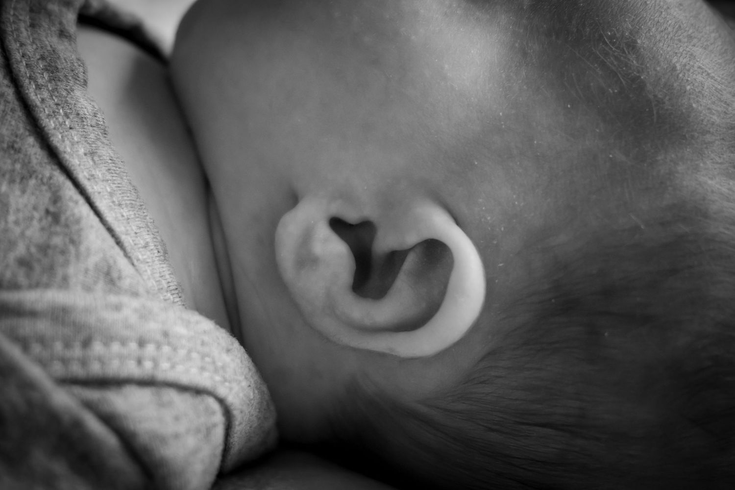 Close-up black and white photo of a newborn baby's delicate ear resting against a parent's chest.