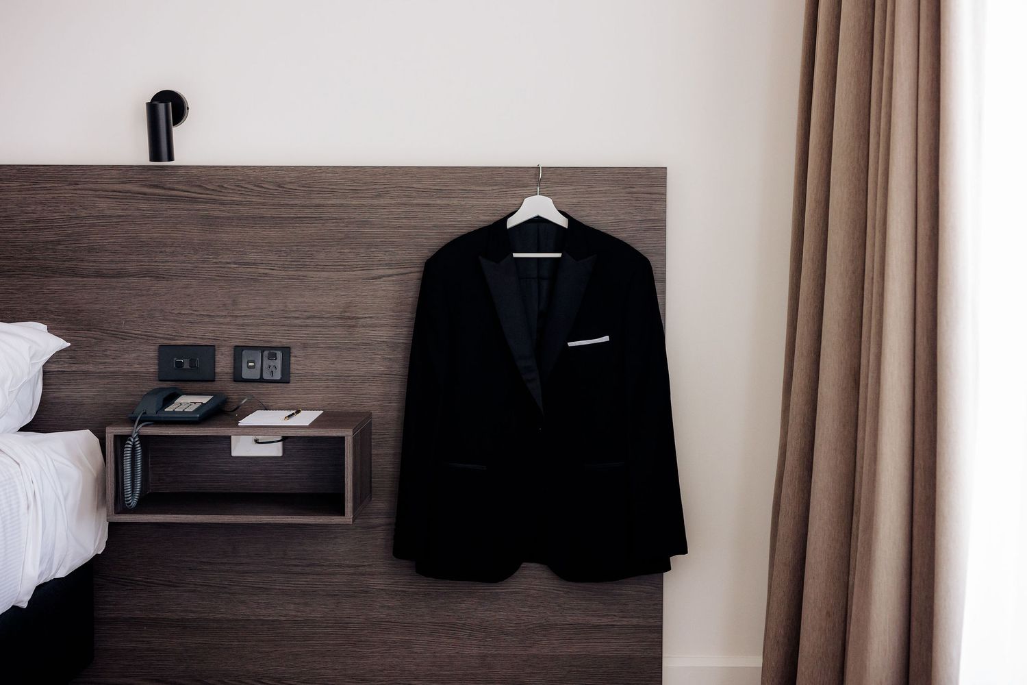 A black t-shirt hangs on a wooden closet rod alongside other clothing items against a neutral wall.