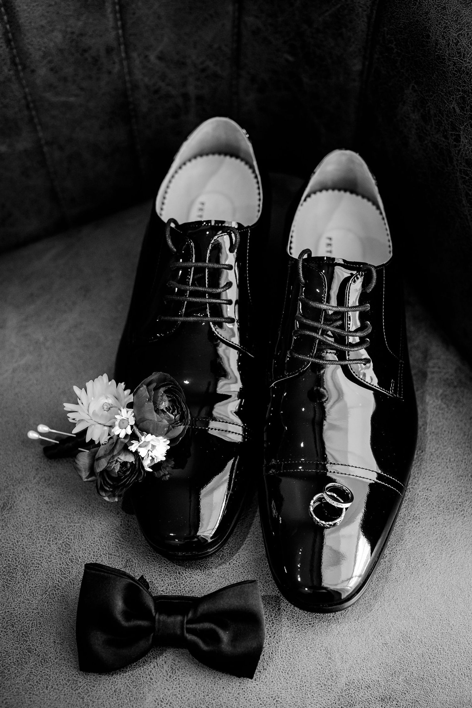 Black and white photo series of patent leather dress shoes with delicate white flowers and bowties arranged against cloth.