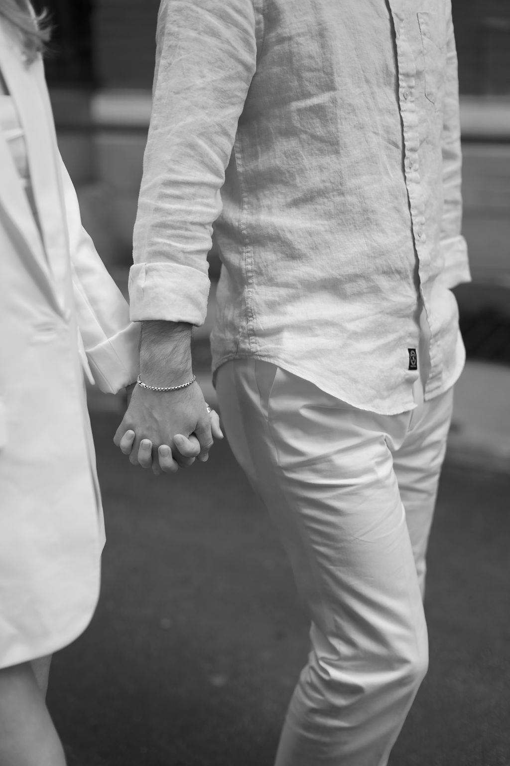 Close-up black and white shot of two people holding hands while walking together.