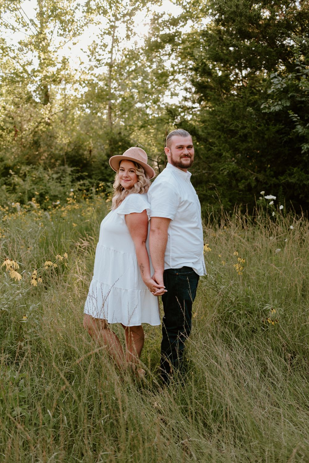 A couple embraces while standing in tall grass during golden hour.