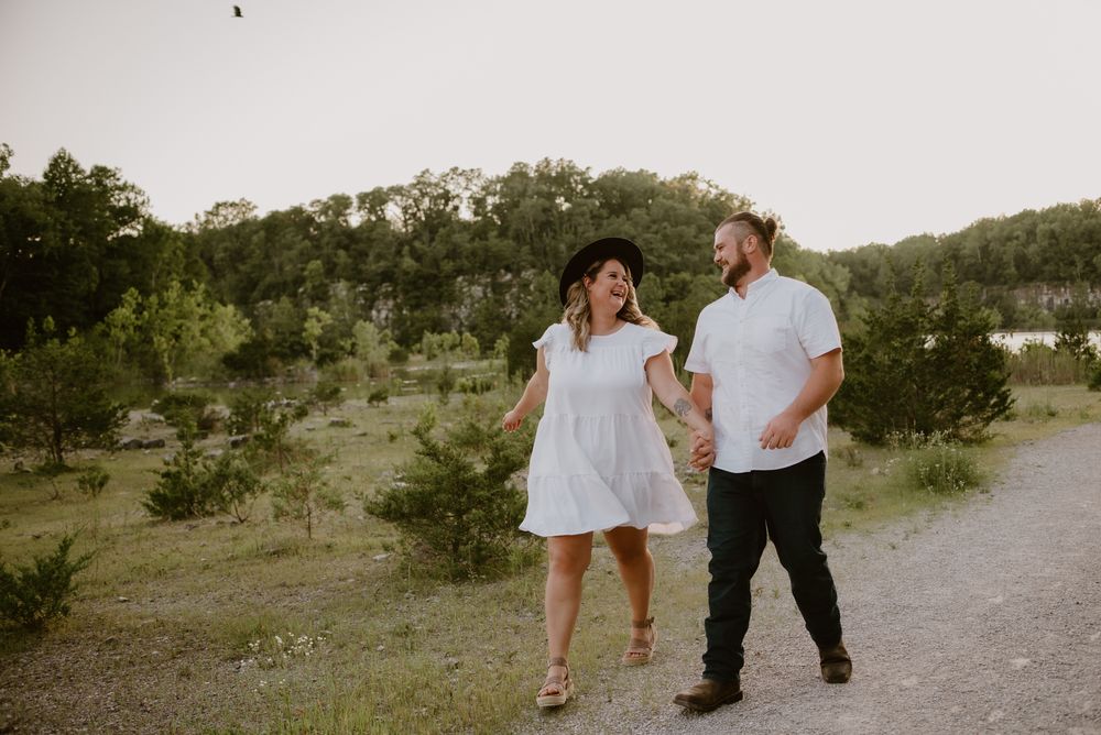 A couple walks hand in hand along a rocky path during a sunset photoshoot.