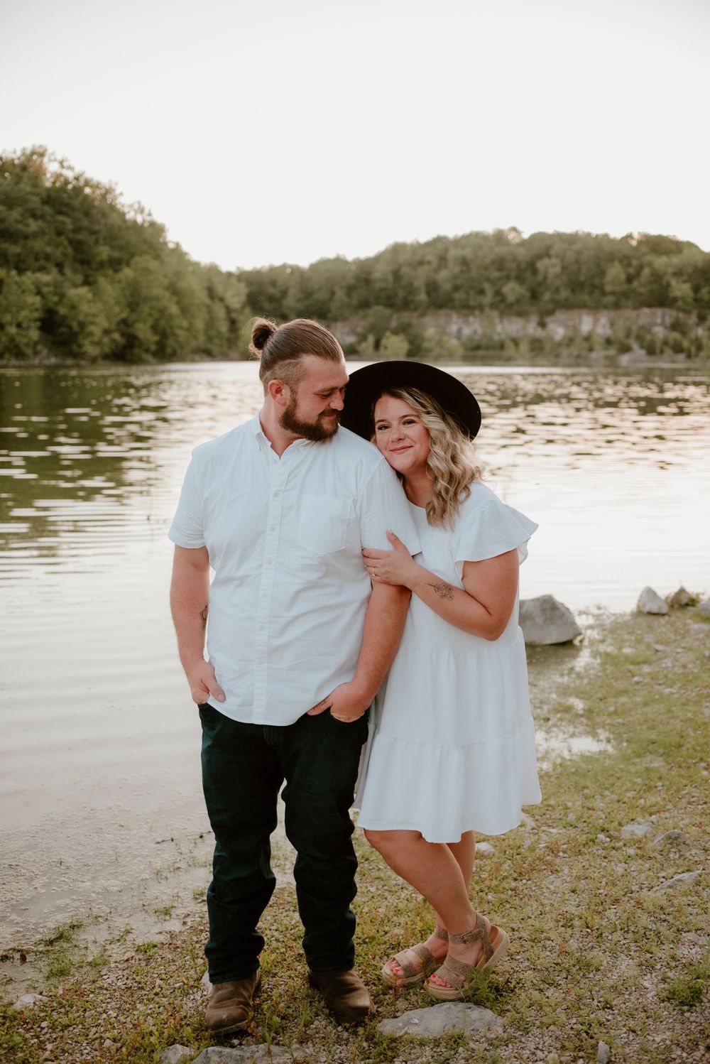 A couple in white outfits shares a romantic moment by a serene lakeside.