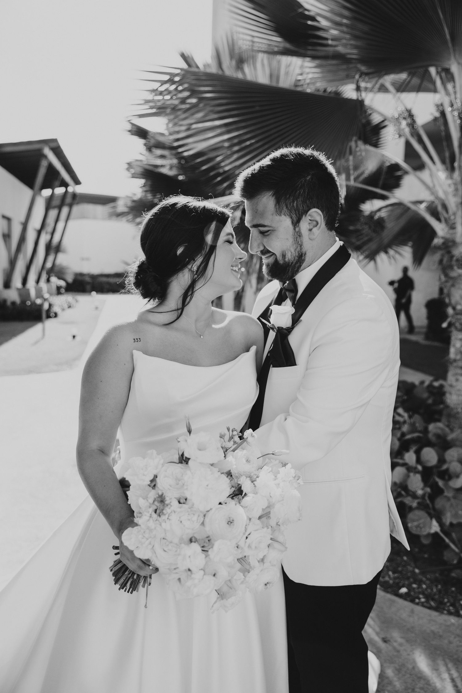 Black and white portrait of newlyweds with palm trees and white bouquet.