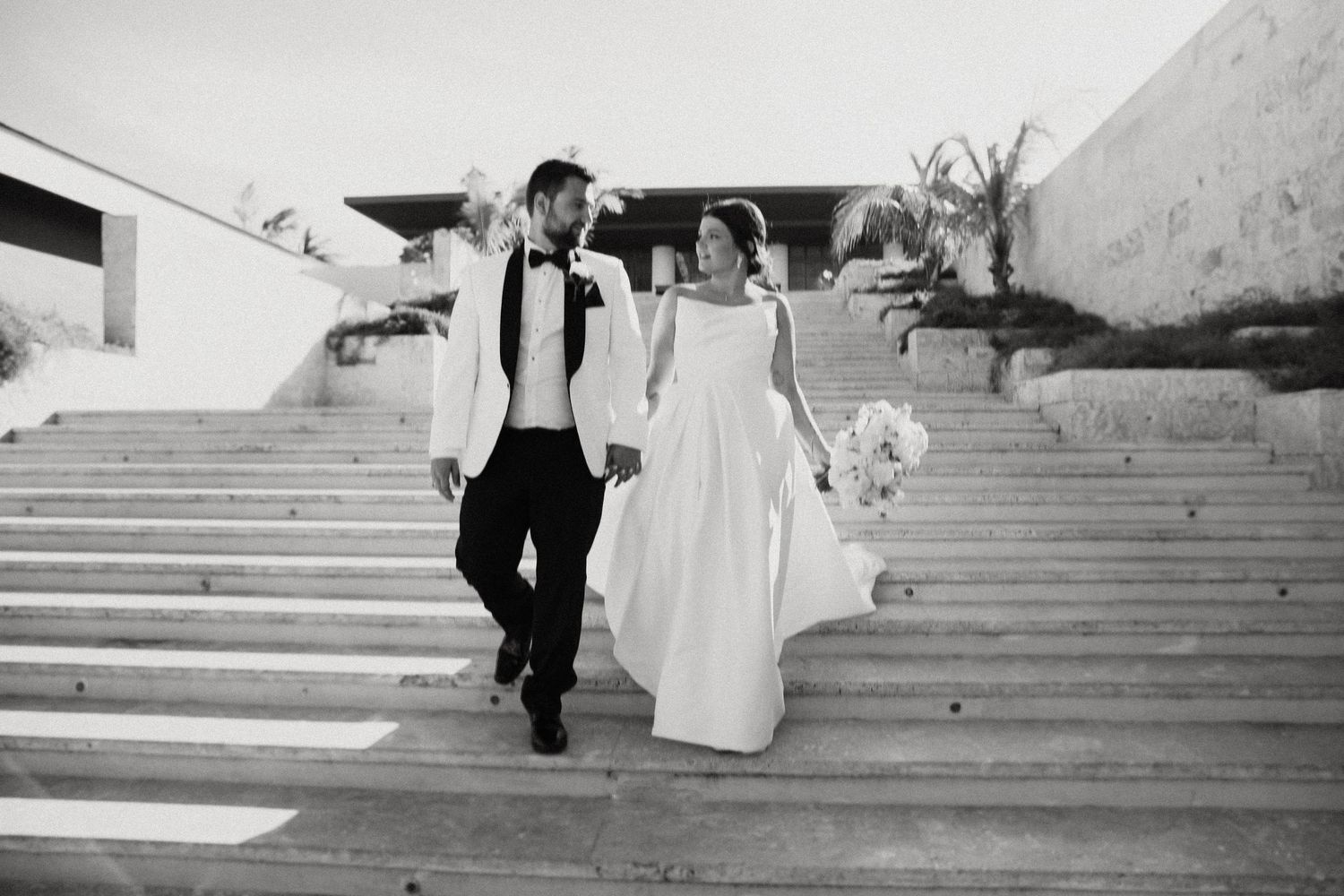 Black and white photo of newlyweds descending stone steps together at Dreams Macao beach resort