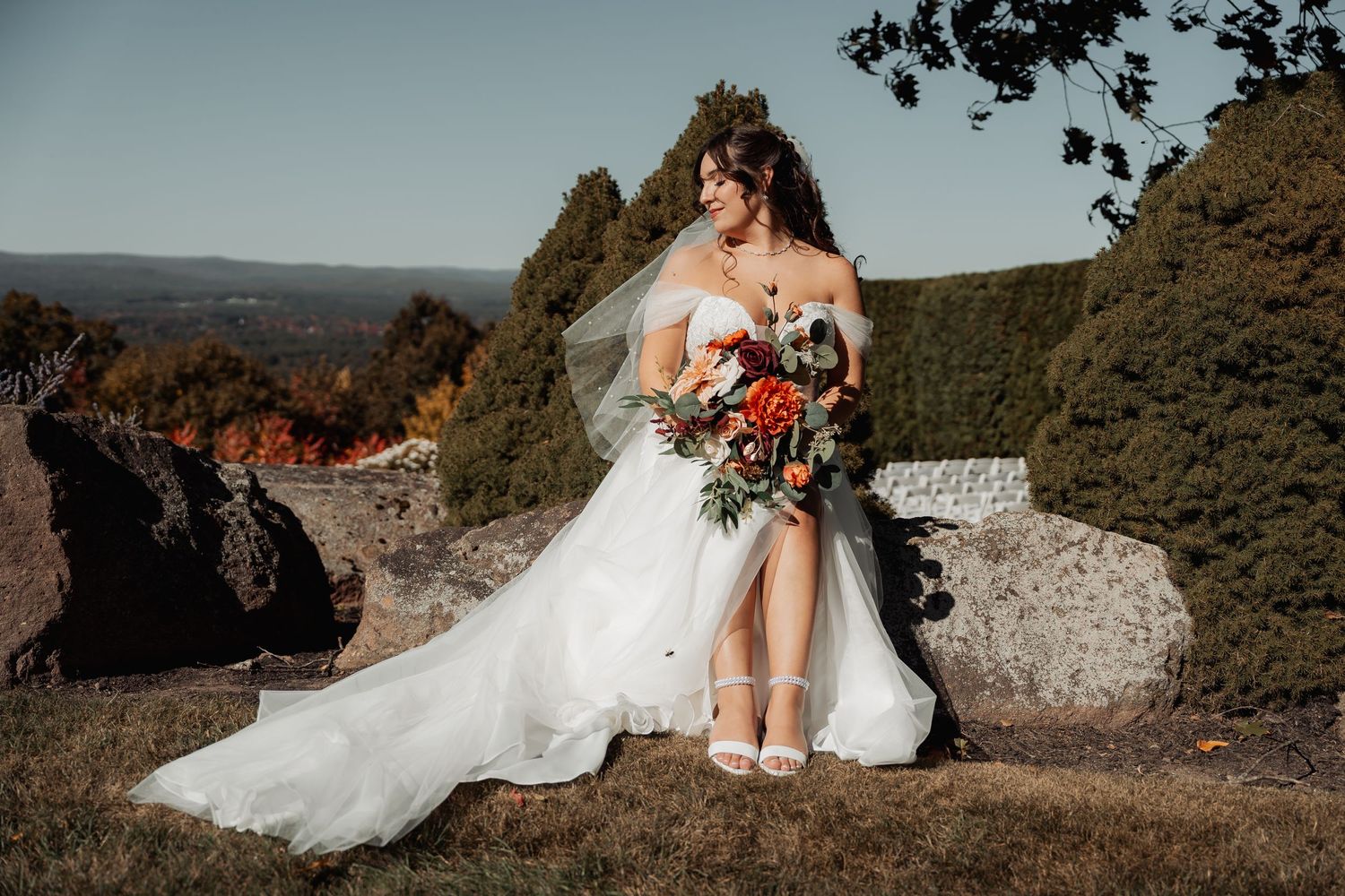 A stunning wedding portrait shows a bride in white perched gracefully on rocky cliffs with mountain views.