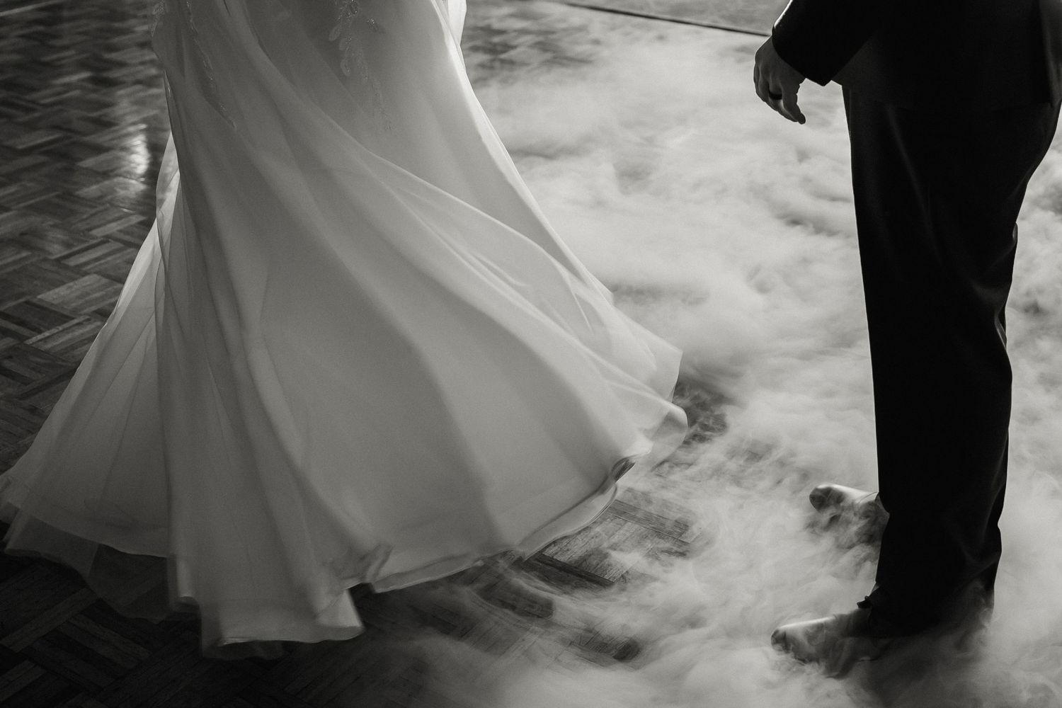 Black and white photo of dancing feet at a wedding with billowing dress and smoke effects.