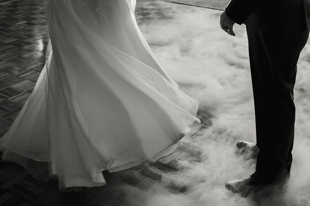 Black and white photo of dancing feet at a wedding with billowing dress and smoke effects.