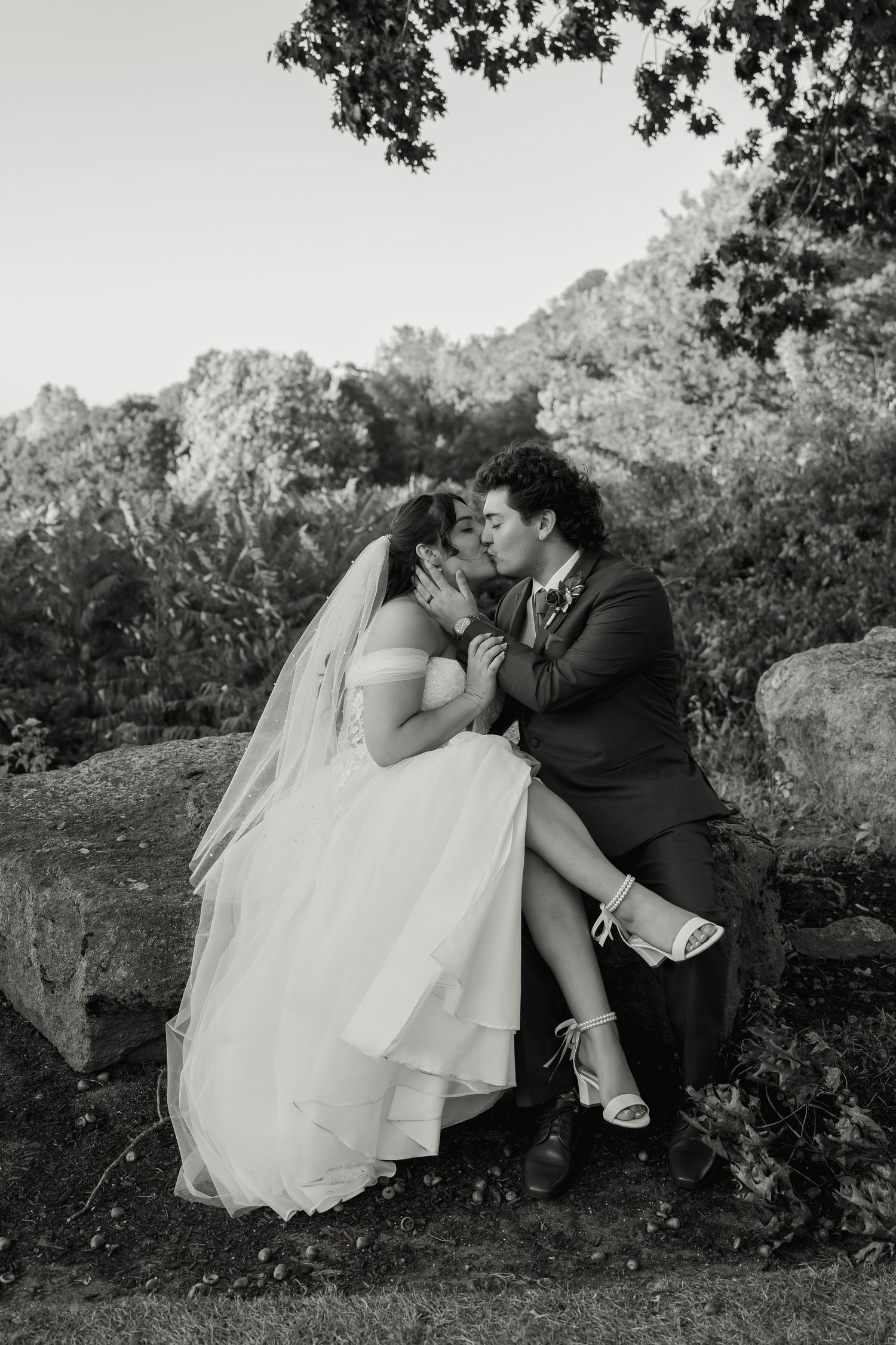 Black and white portrait of couple sharing intimate moment on stone wall.
