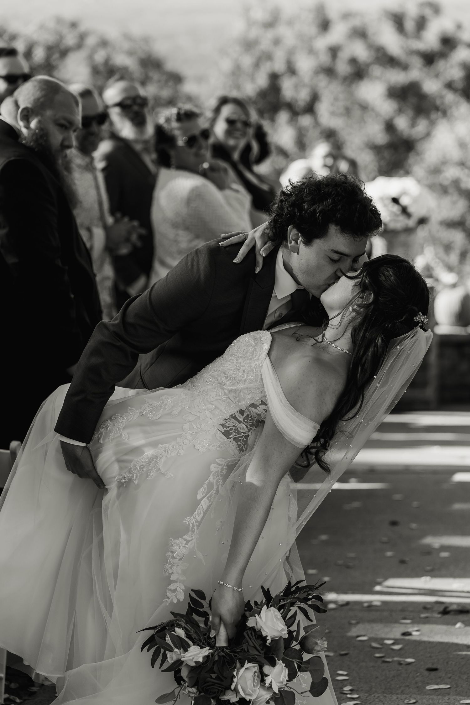 A romantic black and white dip kiss moment during an outdoor wedding ceremony.