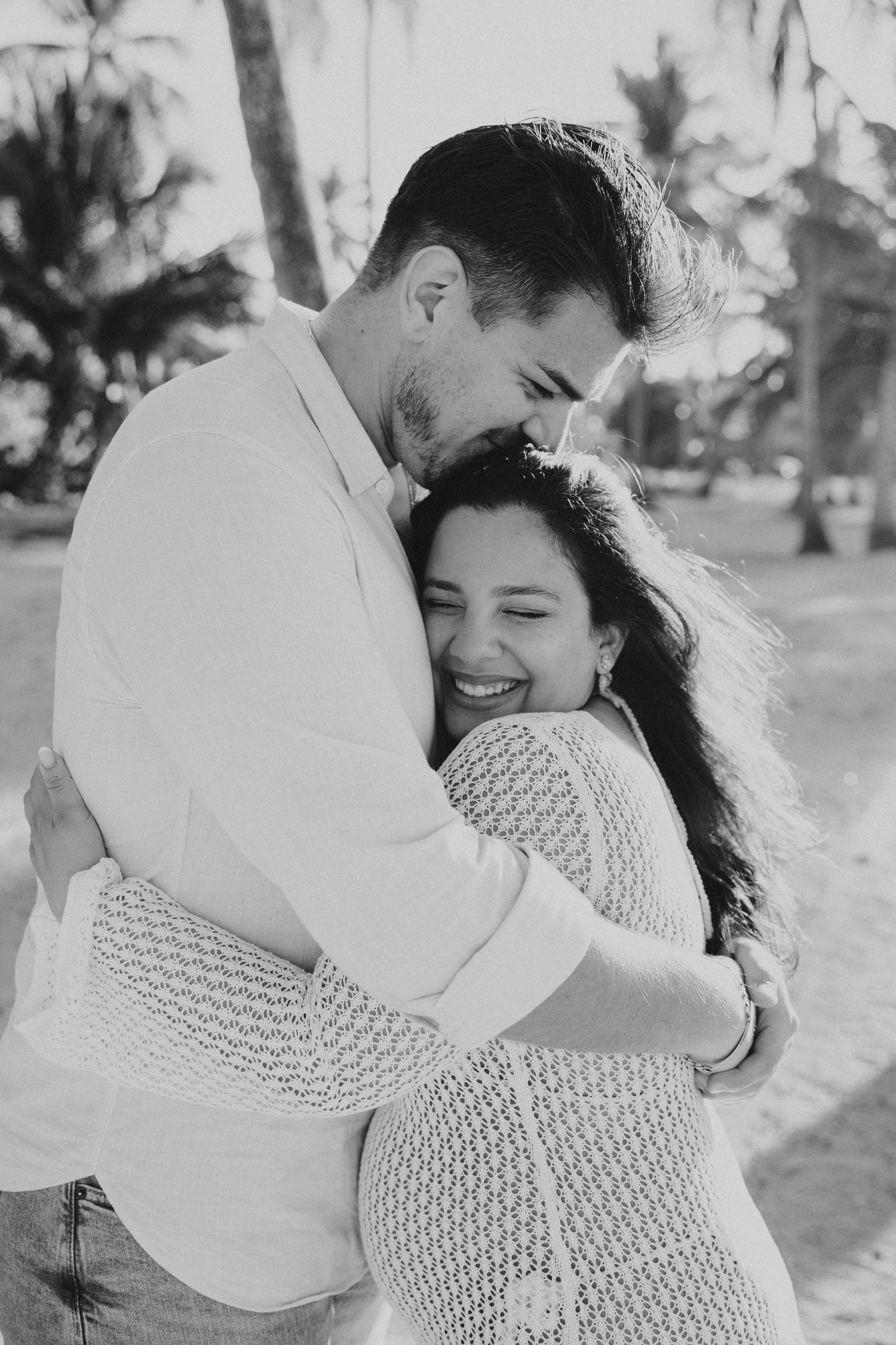 A black and white photo of a couple sharing a loving embrace among palm trees.