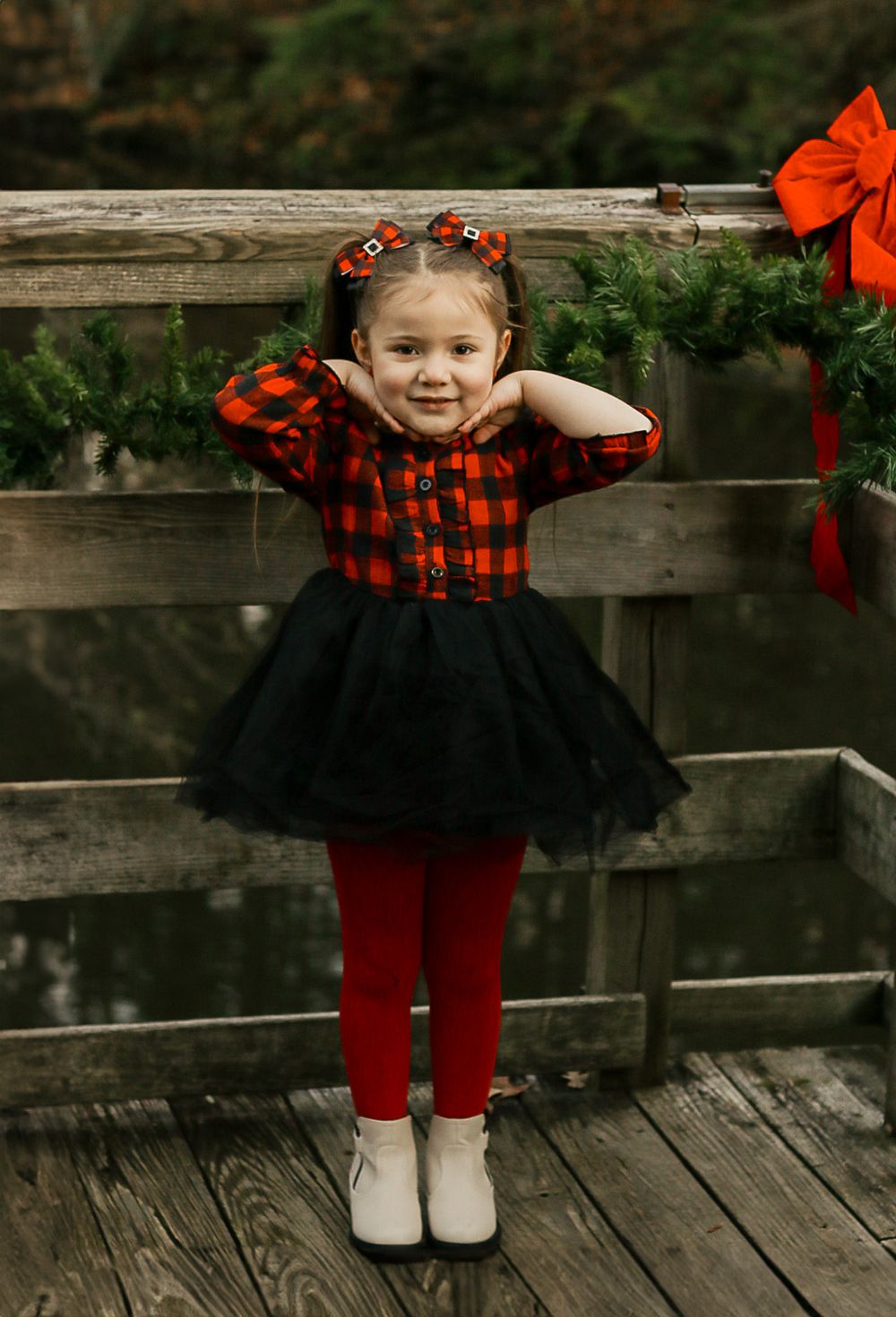 A small figure in a red plaid and black tutu dress stands on a wooden deck.