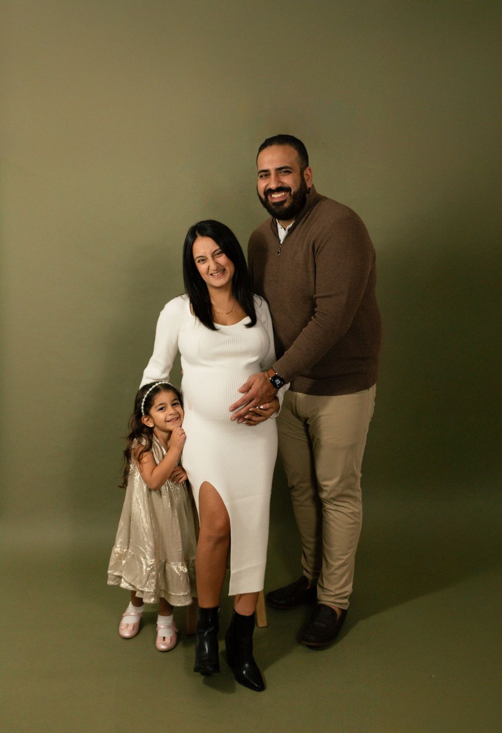 A family portrait against a dark green backdrop wearing coordinated neutral-toned outfits.