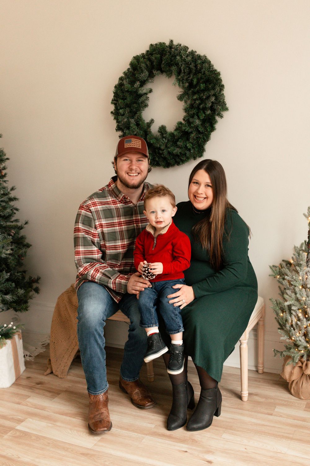 Family poses together in coordinated winter outfits against a neutral backdrop with holiday decor and wooden flooring.