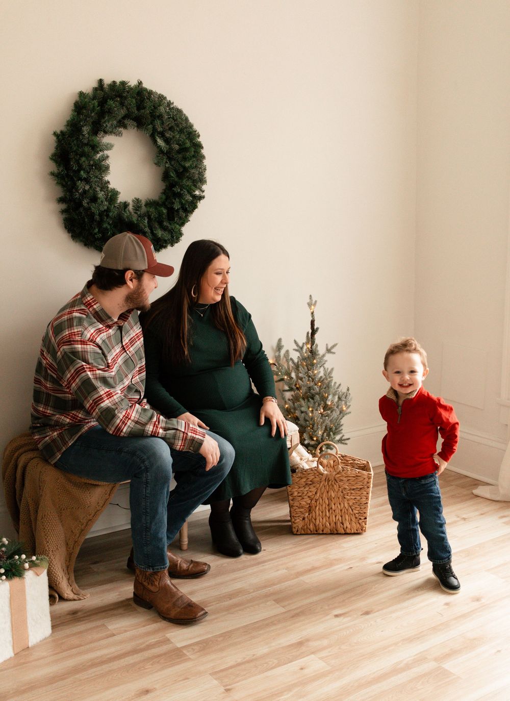 Family shares joyful holiday moment with evergreen wreath and small Christmas tree in minimalist indoor setting.