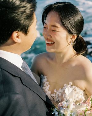 A joyful couple shares a close intimate moment while dressed in wedding attire against a soft blue sky background.