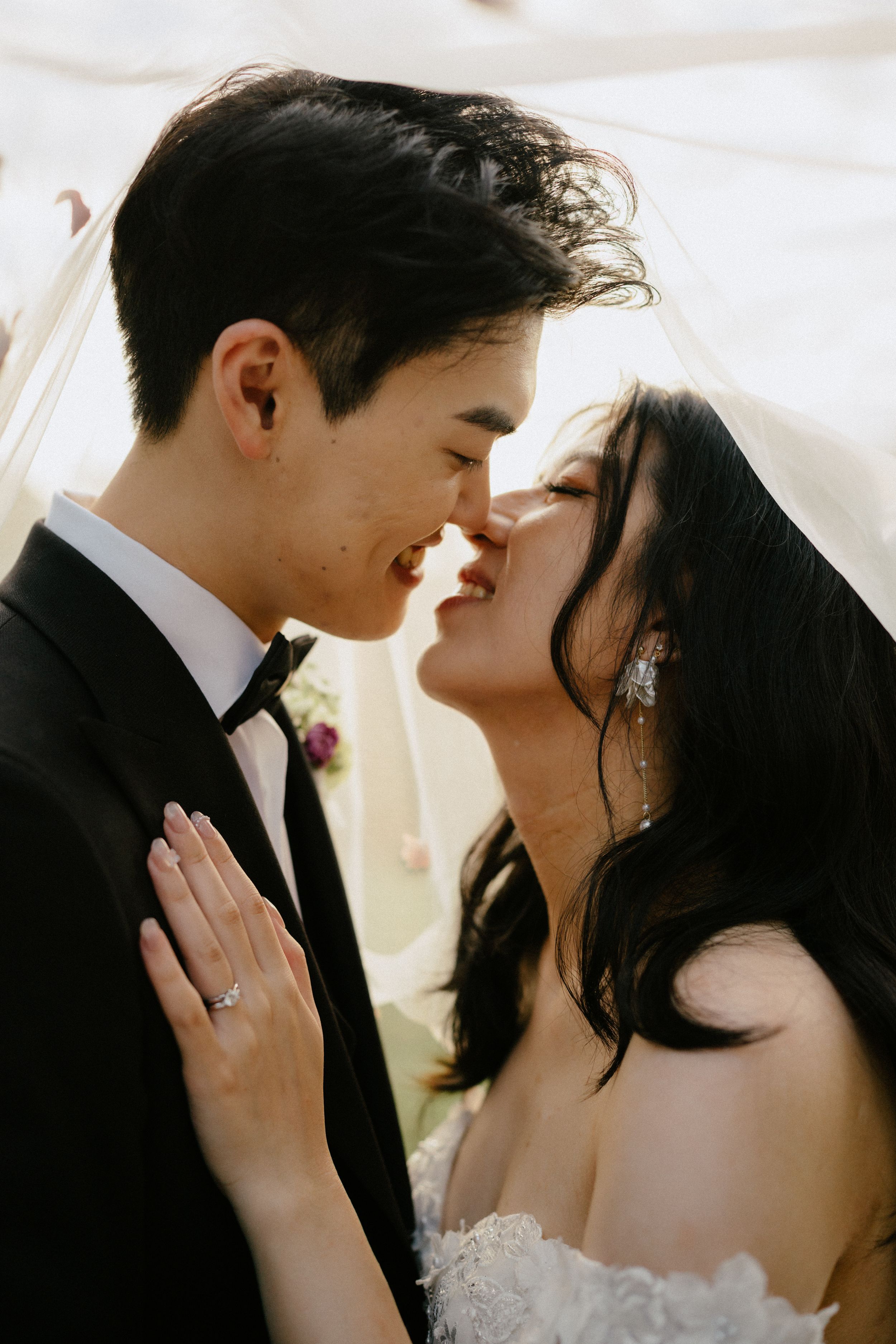 A romantic wedding portrait of a couple in formalwear sharing an intimate moment in soft sunlight.