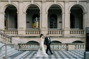 A couple in wedding attire walking through an ornate colonnade hallway in an elegant historic building.