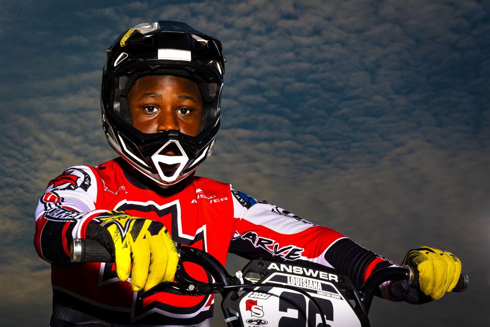 Group of professional motocross riders racing on dirt track wearing protective gear and helmets.