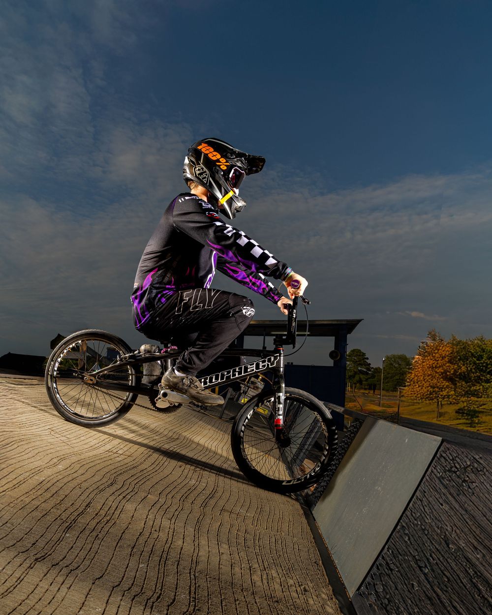 BMX rider performs a trick on a wooden ramp at sunset with a dramatic sky backdrop.