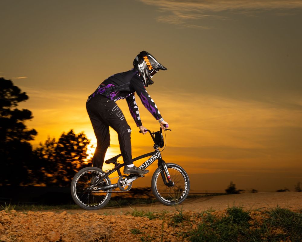 Mountain biker silhouetted against dramatic orange sunset sky performing sequential jump progression on dirt trail.