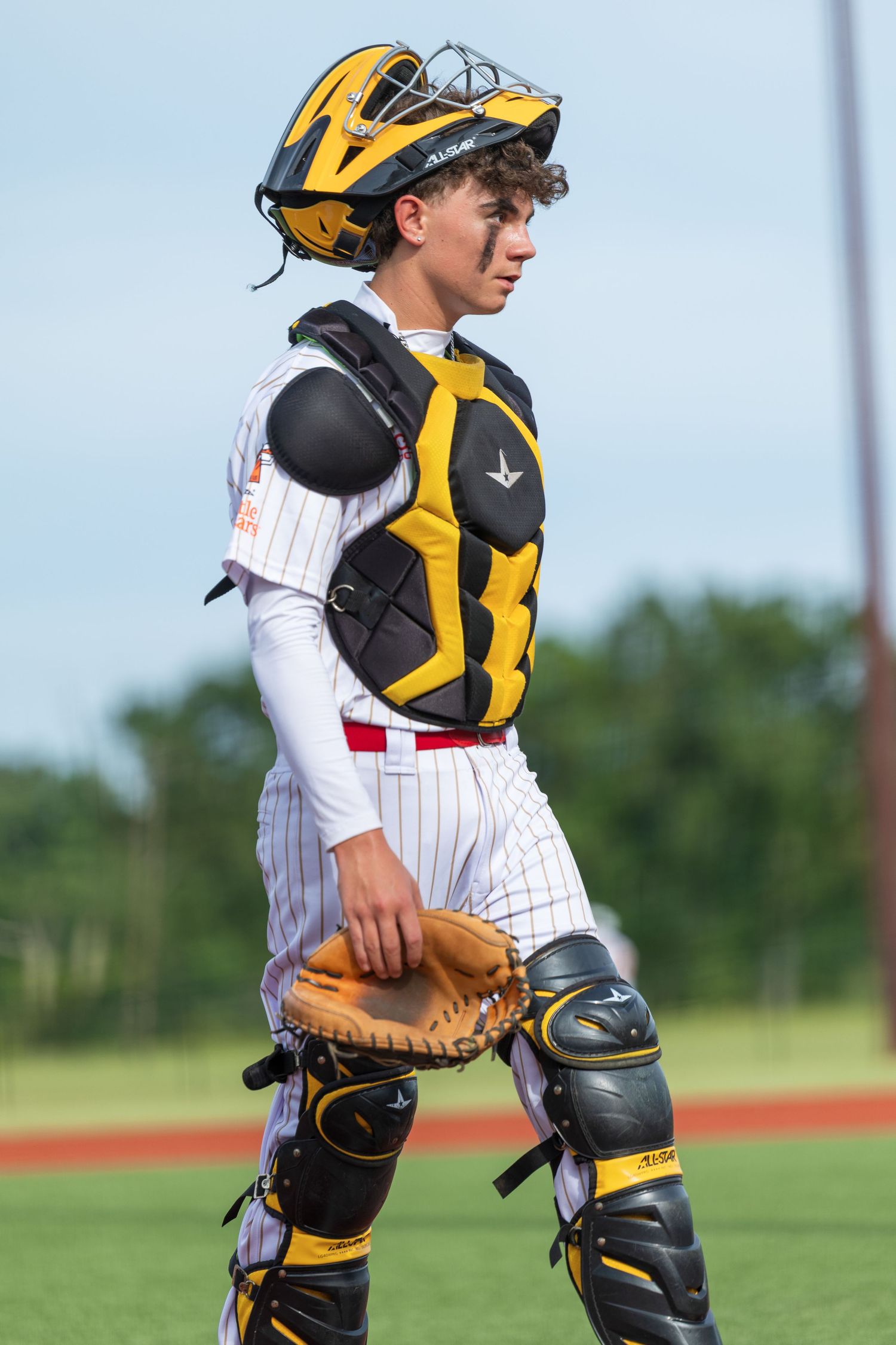 Young baseball catcher in yellow and black protective gear holding mitt on a sunny field.