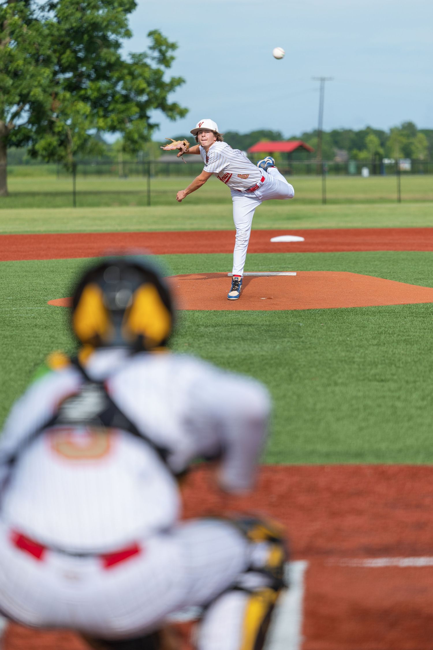 Young baseball pitcher throwing ball from mound as catcher waits in foreground during youth league game.