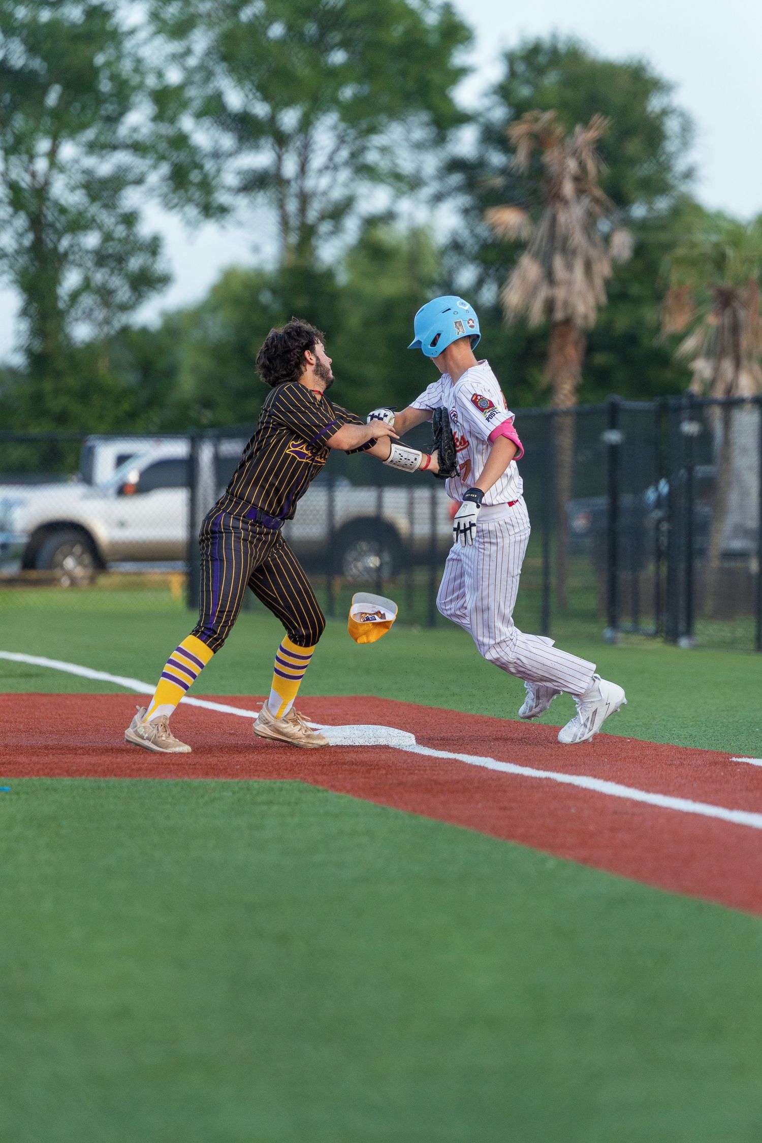 Baseball player in blue helmet runs to first base as fielder attempts a tag during an outdoor game.