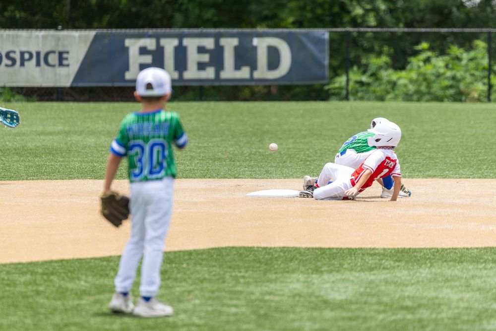 Youth baseball players compete on a field, with one player sliding into base during a little league game.