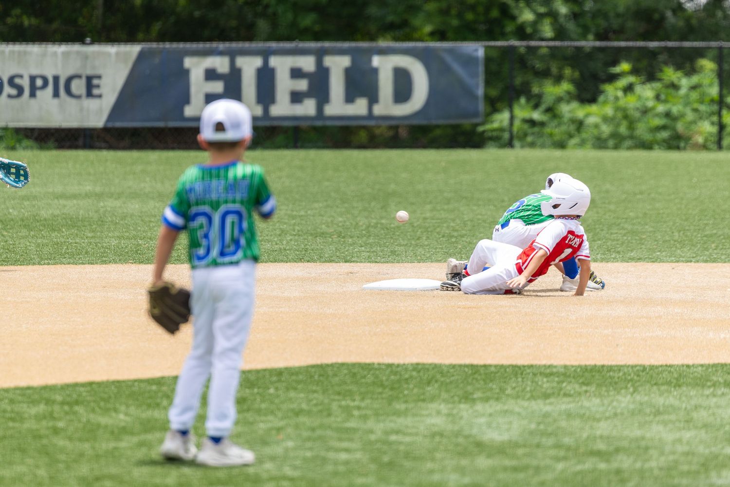 Youth baseball players compete on a field, with one player sliding into base during a little league game.